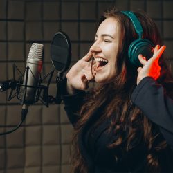 Female person records POP song at the recording studio. Singer emotionally gesturing with her hands. Soundproof room for professional recording vocal